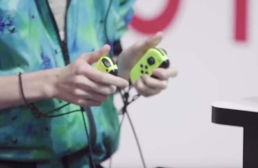 Se aprecian unos Joy Con conectados por cable a un soporte de carga en un vídeo del Nintendo Live 2018